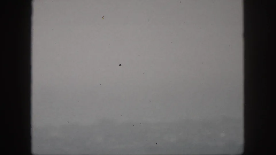 1959 Hawaii home-movie frame with a faint mountain ridge, gray overcast sky, and dark viewfinder-like edges.