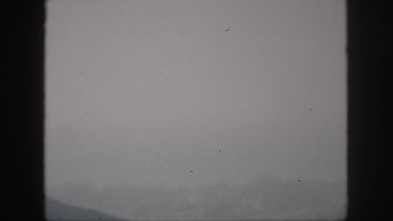 1959 Oahu 8mm frame showing a faint misty mountain ridge under a gray sky, with dark frame-edge shadows and soft exposure.