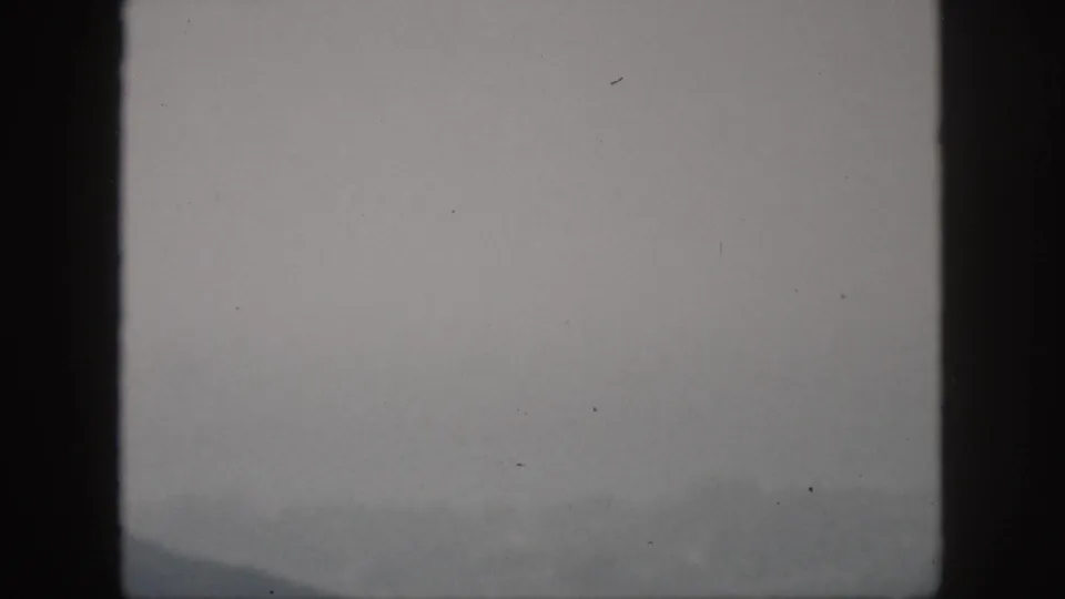 1959 Oahu 8mm frame showing a faint misty mountain ridge under a gray sky, with dark frame-edge shadows and soft exposure.