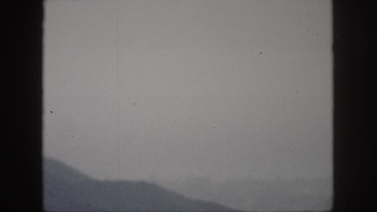 Dark sloping mountain silhouette under a pale gray sky, partly obscured by film borders.