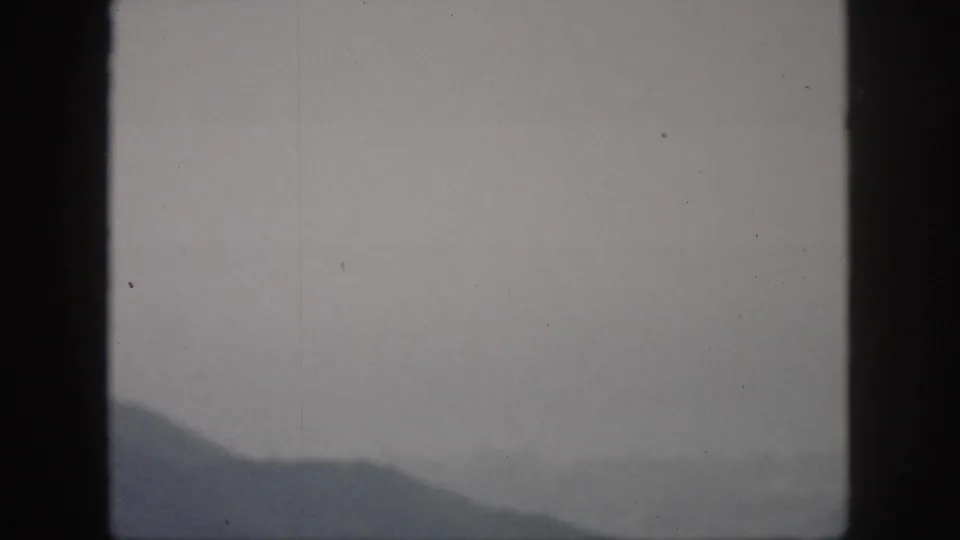 1959 Oahu home-movie frame with a sloping mountain silhouette seen through haze beneath a muted gray sky.