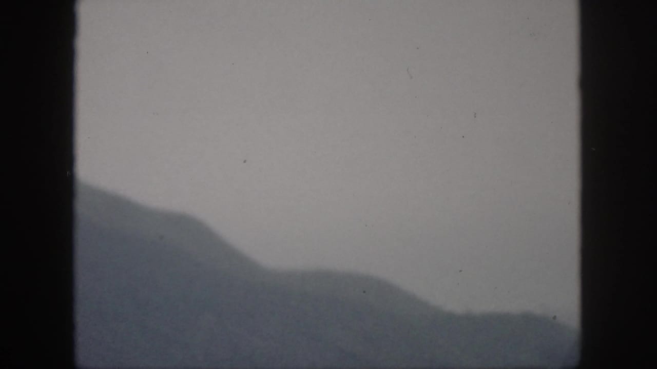 1959 Oahu 8mm frame showing layered misty hills and a low ridgeline under an overcast sky.