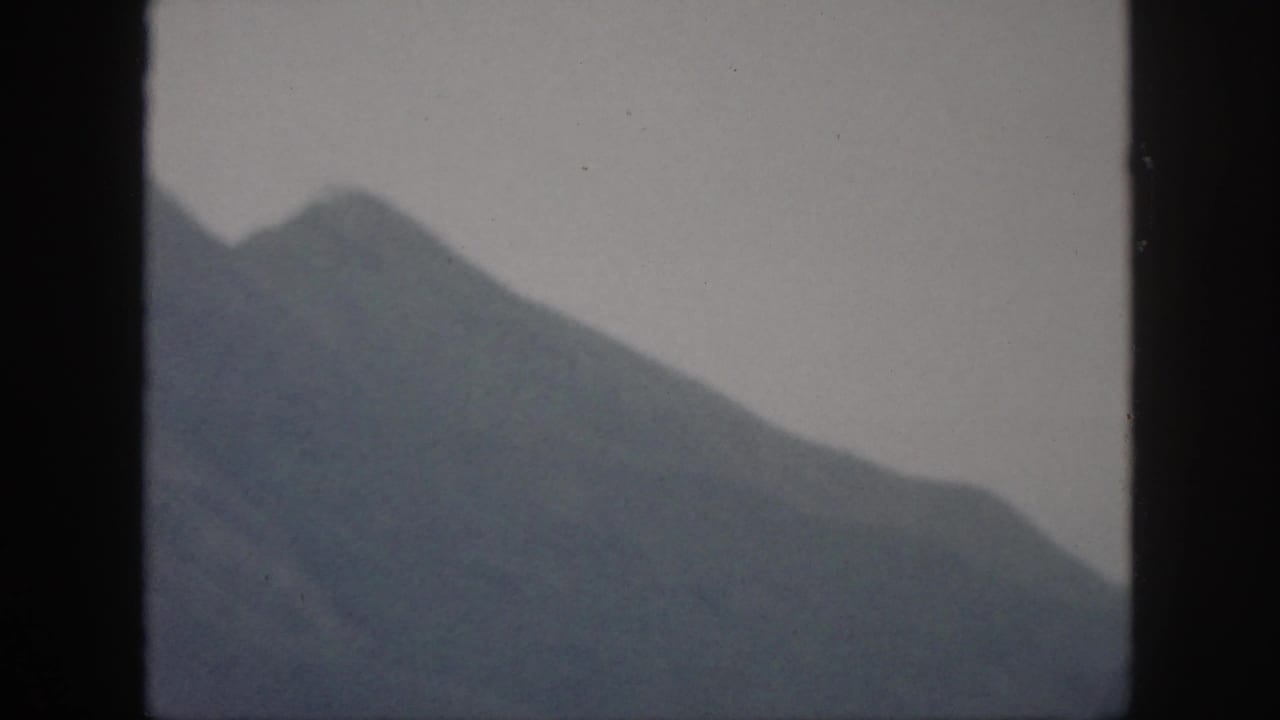 1959 Oahu home-movie frame showing a broad dark mountain ridge and peaked slope softened by haze.
