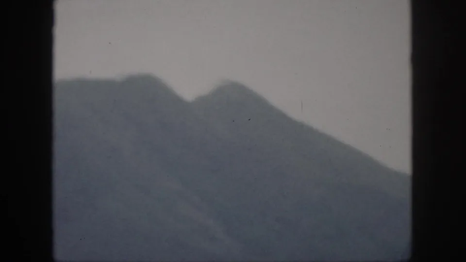 1959 Oahu home-movie frame showing distant rugged mountain peaks beneath a hazy, pale sky, bordered by the 8mm film scan.