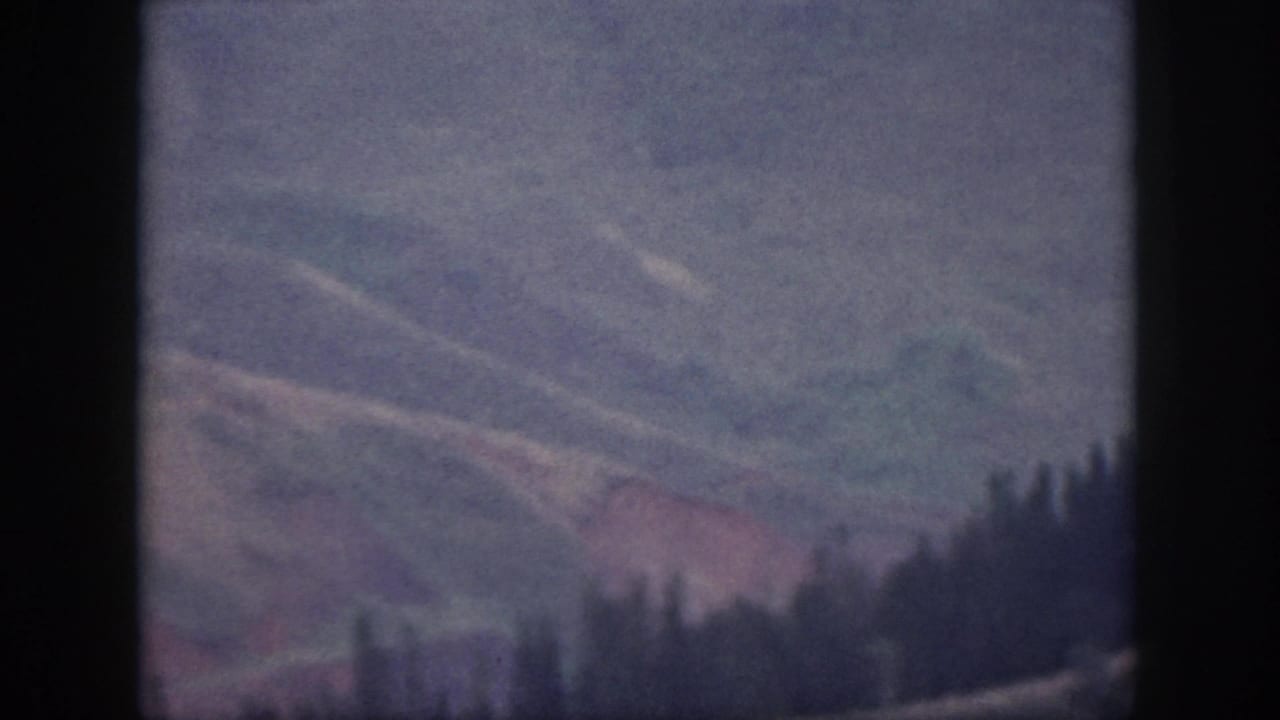 1959 Oahu mountain terrain with pale ridges, reddish soil tones, and a dark tree-lined crest.