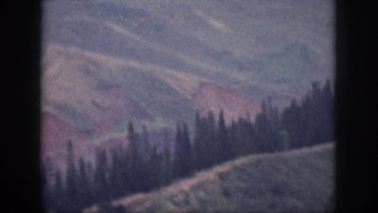Vintage 8mm view of Oahu mountain slopes, with dark trees across the crest and muted red earth tones.