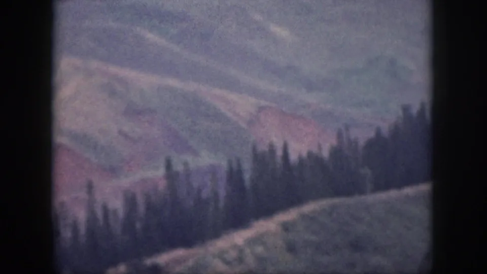 Vintage 8mm view of Oahu mountain slopes, with dark trees across the crest and muted red earth tones.