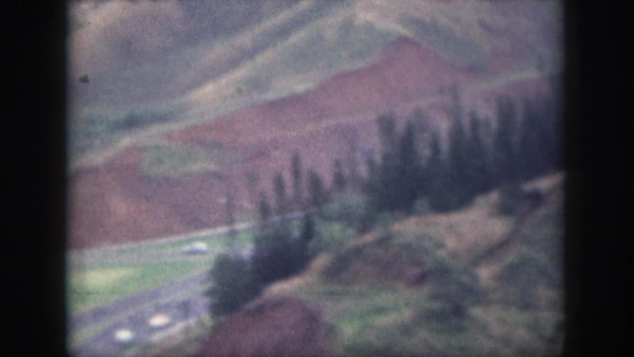 1959 Oahu 8mm frame showing a road curving through rolling hills, reddish earth, green patches, and small cars below.