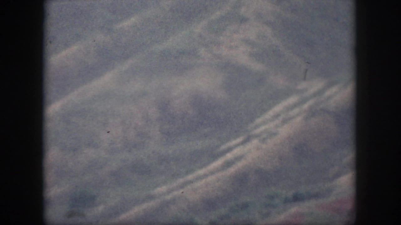 Soft 8mm frame from Oahu showing hazy rolling hills, diagonal road lines, muted vegetation, and no visible people.