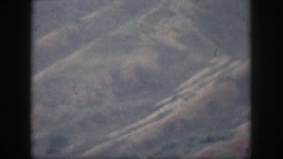 Soft 8mm frame from Oahu showing hazy rolling hills, diagonal road lines, muted vegetation, and no visible people.