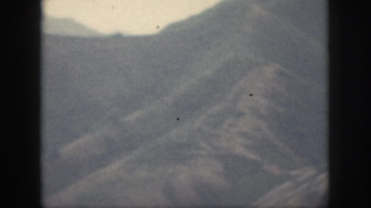 1959 Oahu 8mm frame with distant hazy hills, pale sky, soft ridgelines, and faint vegetation across the slopes.