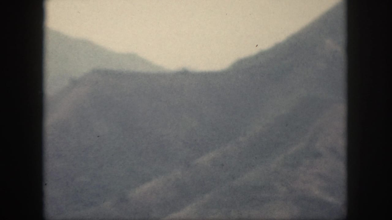 1959 Oahu 8mm frame showing hazy layered mountain ridges under a pale sky, with soft focus and dark film edges.
