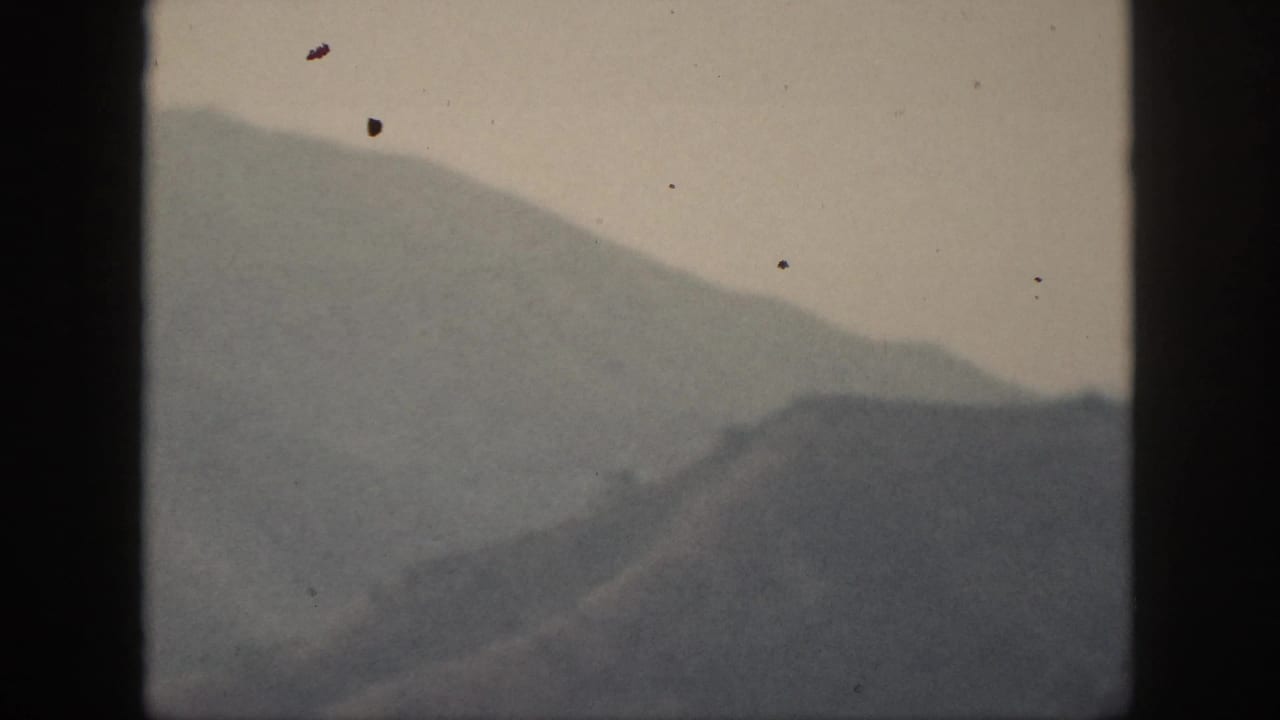 Hazy mountain slope and ridge line seen through dust-speckled 8mm film.