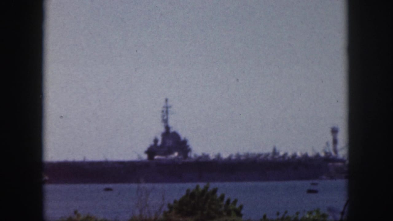 Large naval vessel across harbor water, framed by dark vertical window edges.