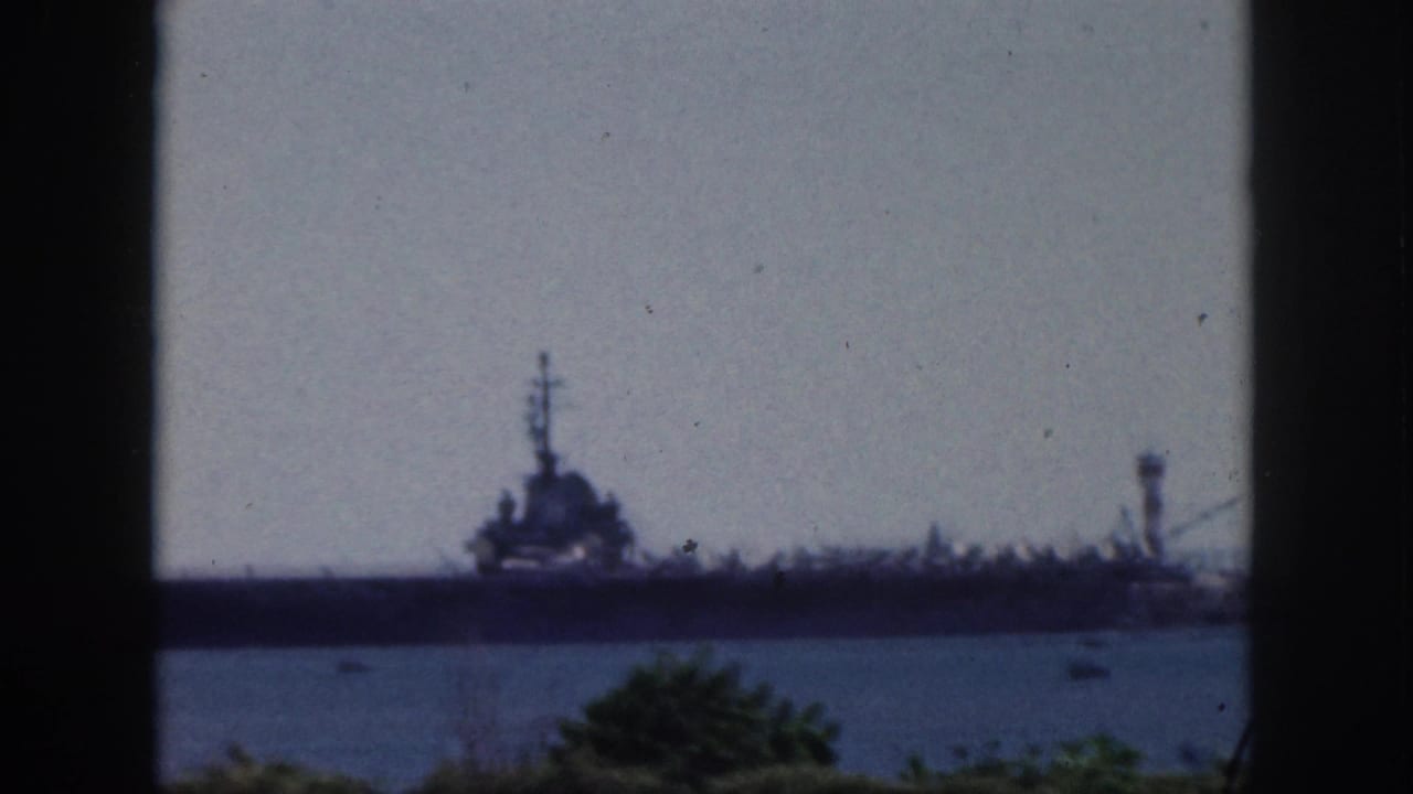 Faded 1959 Oahu harbor view of a large military ship across the water, with small boats and greenery below.