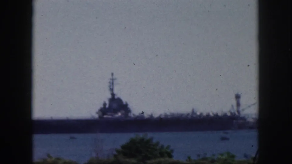 Faded 1959 Oahu harbor view of a large military ship across the water, with small boats and greenery below.