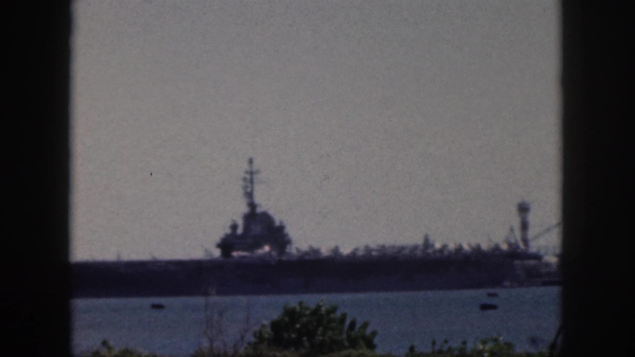 Oahu harbor frame from 1959 showing a large military ship in silhouette, small boats on the water, and vegetation at the lower edge.