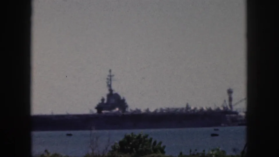 Oahu harbor frame from 1959 showing a large military ship in silhouette, small boats on the water, and vegetation at the lower edge.