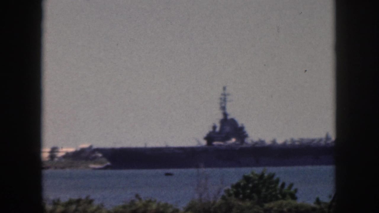 Soft 8mm frame from Oahu, 1959, showing a large naval ship across water through dark vertical and horizontal frame edges.