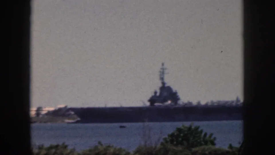 Soft 8mm frame from Oahu, 1959, showing a large naval ship across water through dark vertical and horizontal frame edges.