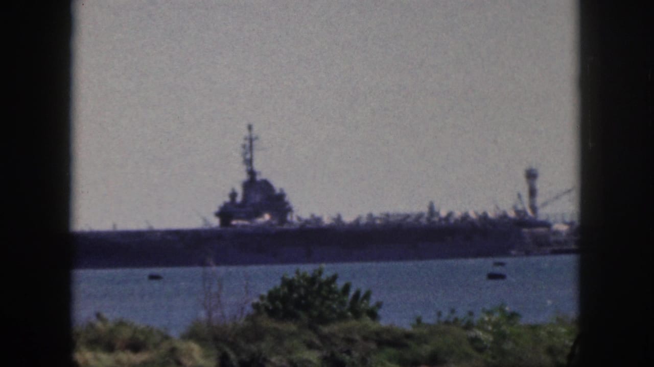 Soft 8mm frame of a naval ship in an Oahu harbor, seen from a shaded interior or doorway with foliage below.