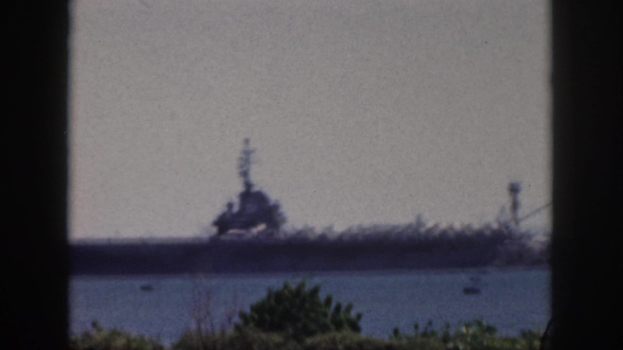 Blurred final frame from 1959 Oahu showing the distant naval ship across harbor water, with small boats, foliage, and dark framing around the view.