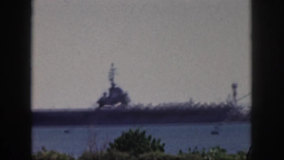 Blurred final frame from 1959 Oahu showing the distant naval ship across harbor water, with small boats, foliage, and dark framing around the view.