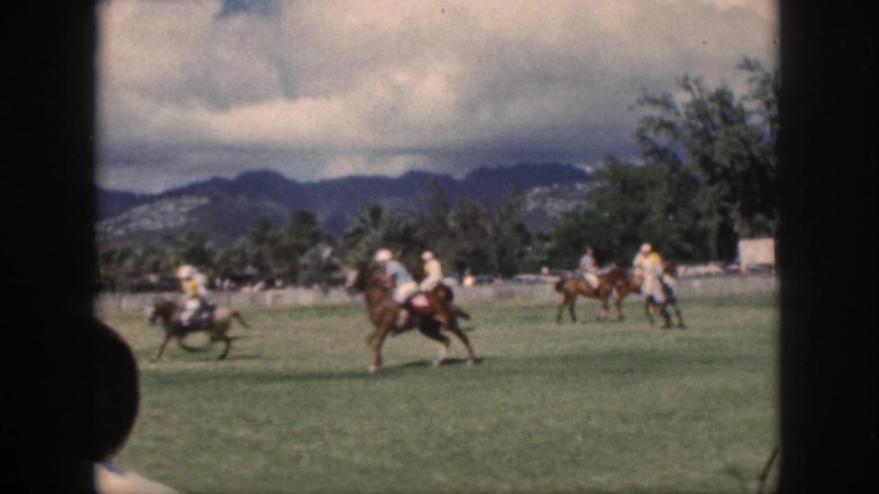 1959 Oahu footage shows mounted polo players moving across a green field below cloudy mountains.
