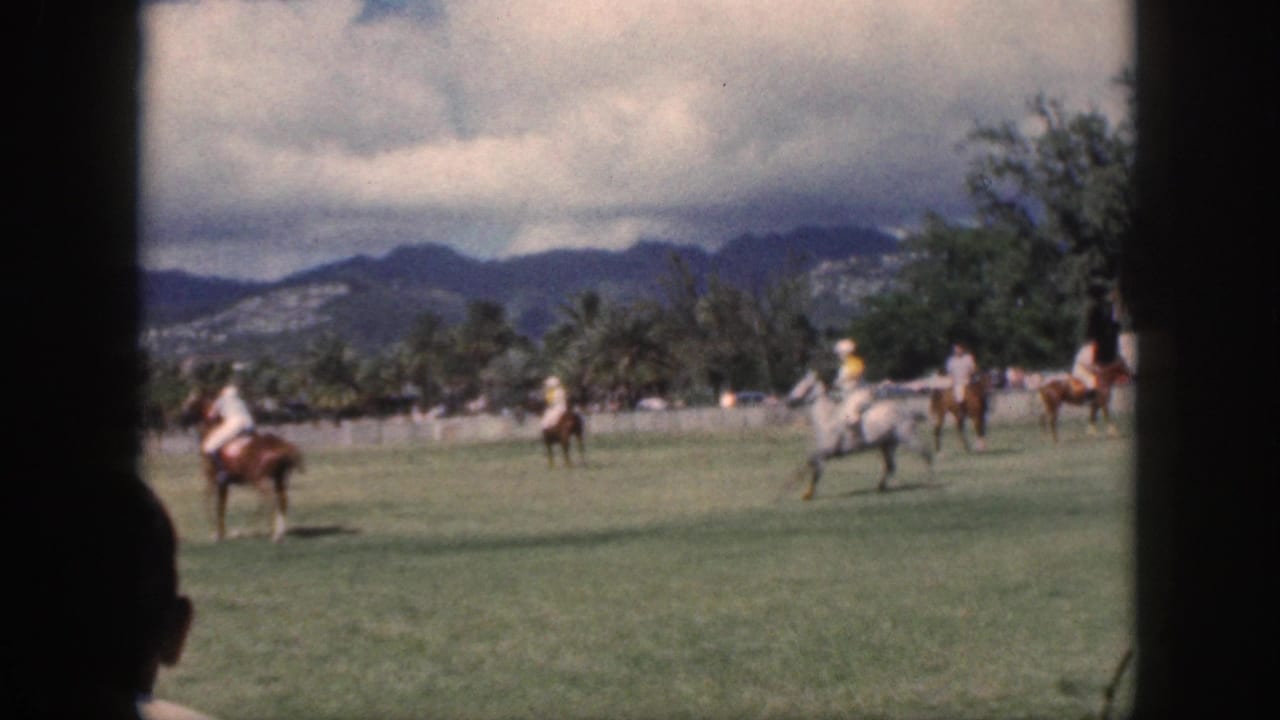1959 Oahu home-movie frame of polo players on horseback spread across the field with mountains beyond.