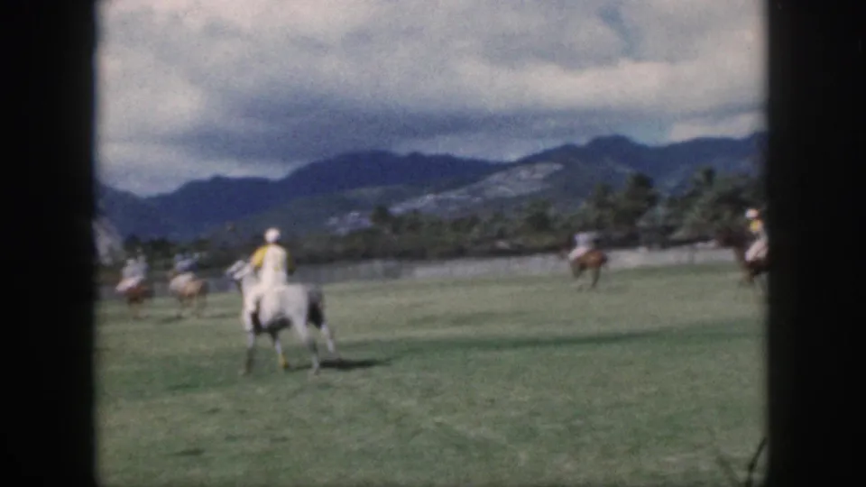 Oahu 1959 home-movie frame with a mounted polo player seen from behind on a grassy field below mountain ridges.