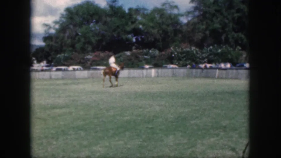 In Oahu, Hawaii home-movie footage from 1959, a rider in a light shirt crosses a broad green field on a brown horse.