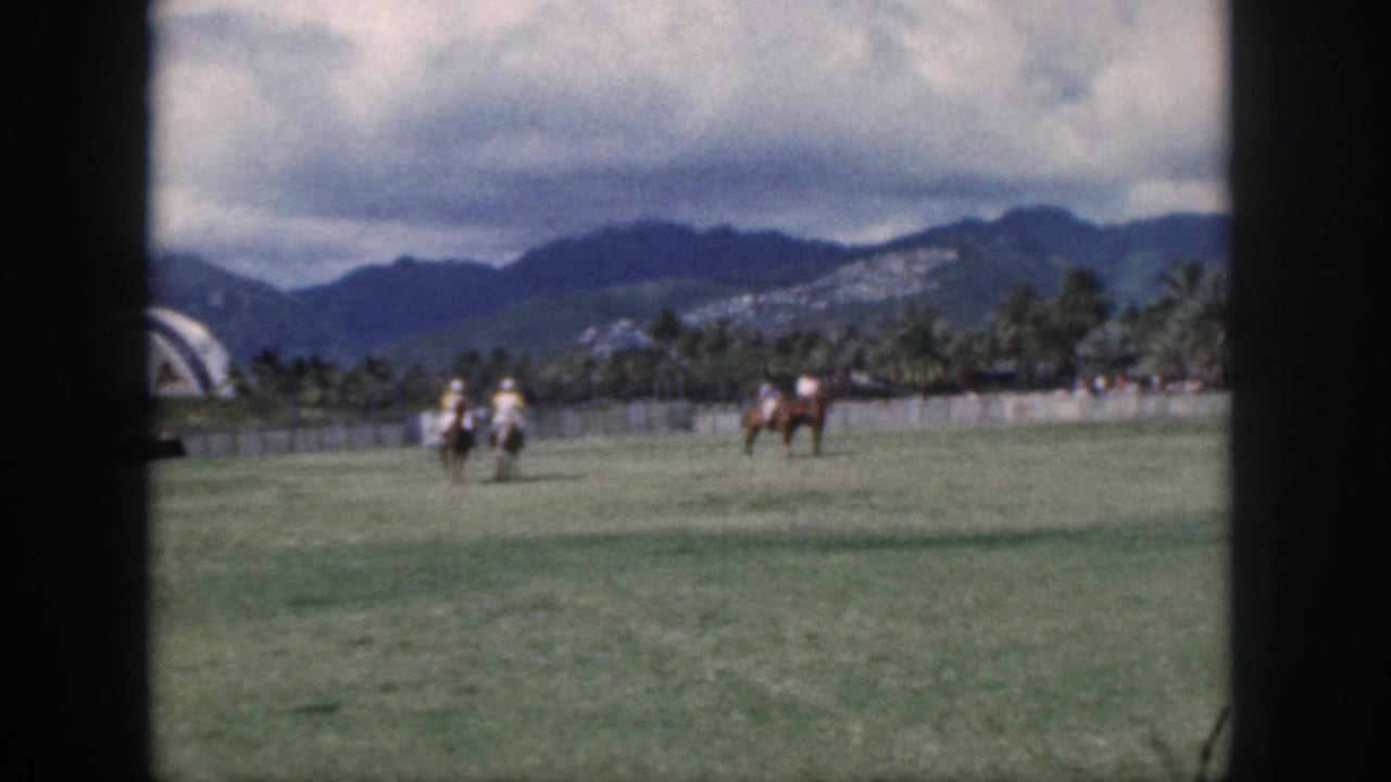 Soft 8mm frame from Oahu in 1959 showing several polo riders grouped on the field with palms and mountains beyond.