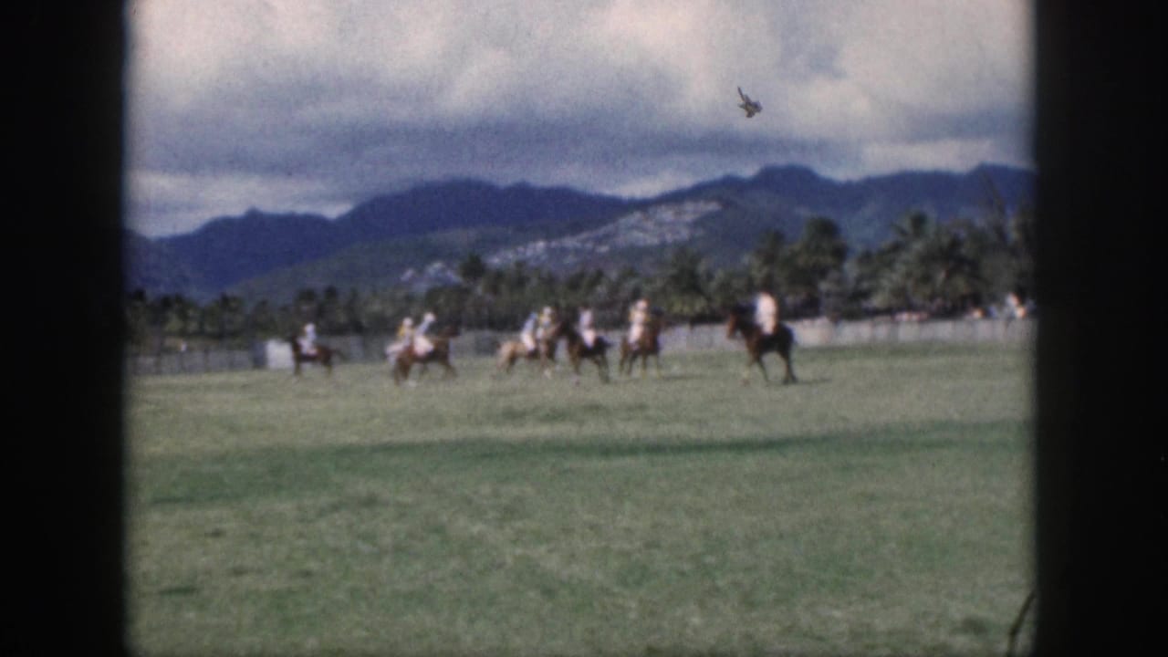 1959 Oahu home-movie frame with polo riders moving across a grassy pitch under a cloudy mountain backdrop.