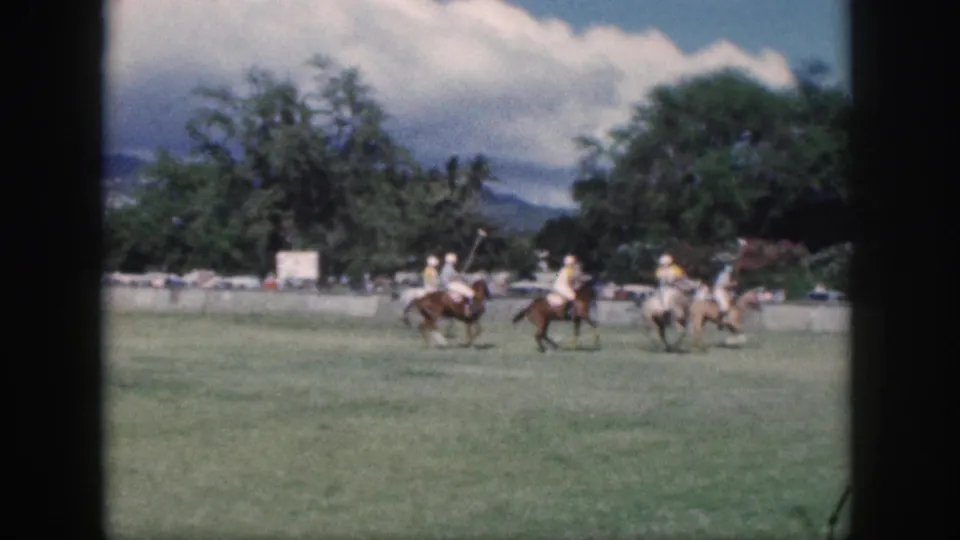 1959 Oahu polo match frame with several riders grouped in play, their mallets visible against the open grass field.