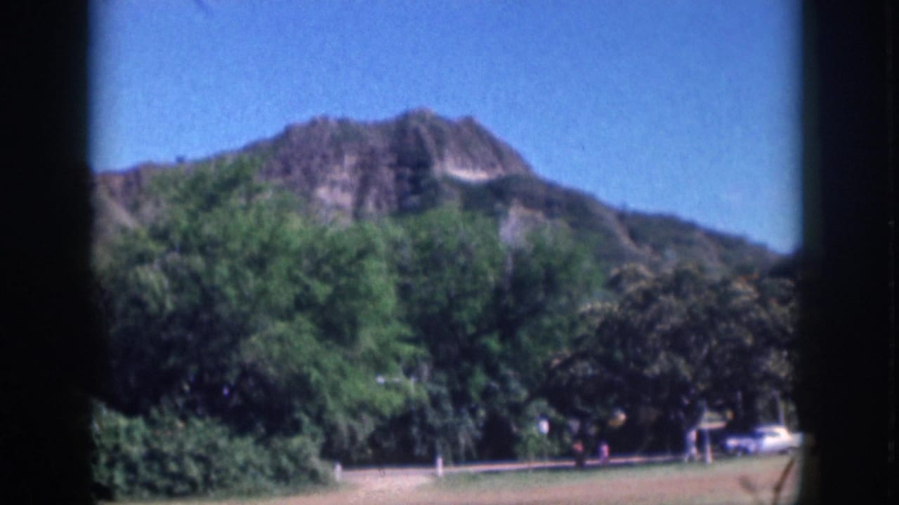 Volcanic hill above green park trees with distant cars and walkers.