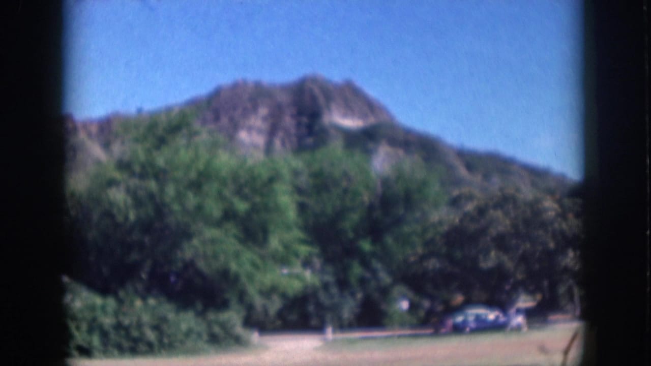 Oahu 1959 park view with lush trees in front of a Diamond Head-like volcanic hill and small parked cars near the path.