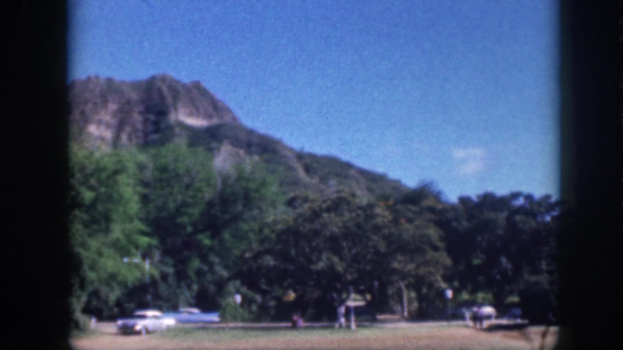 Oahu 1959 home-movie view of a mountain ridge, trees, grass, and parked cars near a recreation area.