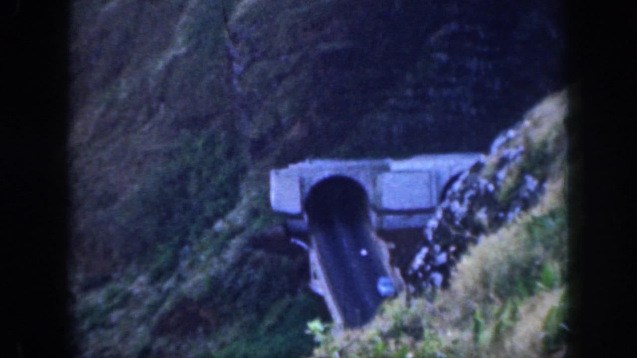 1959 Oahu home-movie frame showing a dark mountain tunnel portal cut into a grassy hillside near a narrow road.