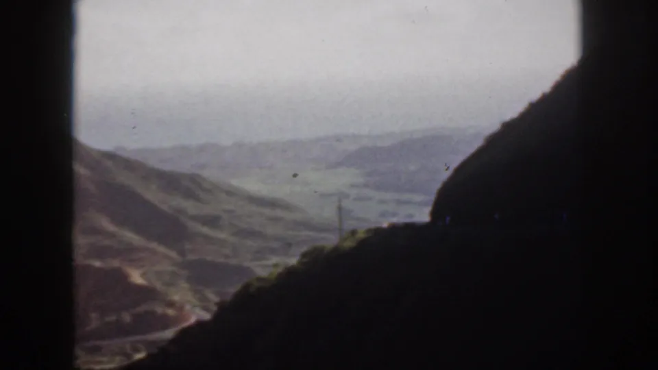 1959 Oahu home-movie view of hilly green terrain and a valley framed by dark roadside or tunnel shadows.