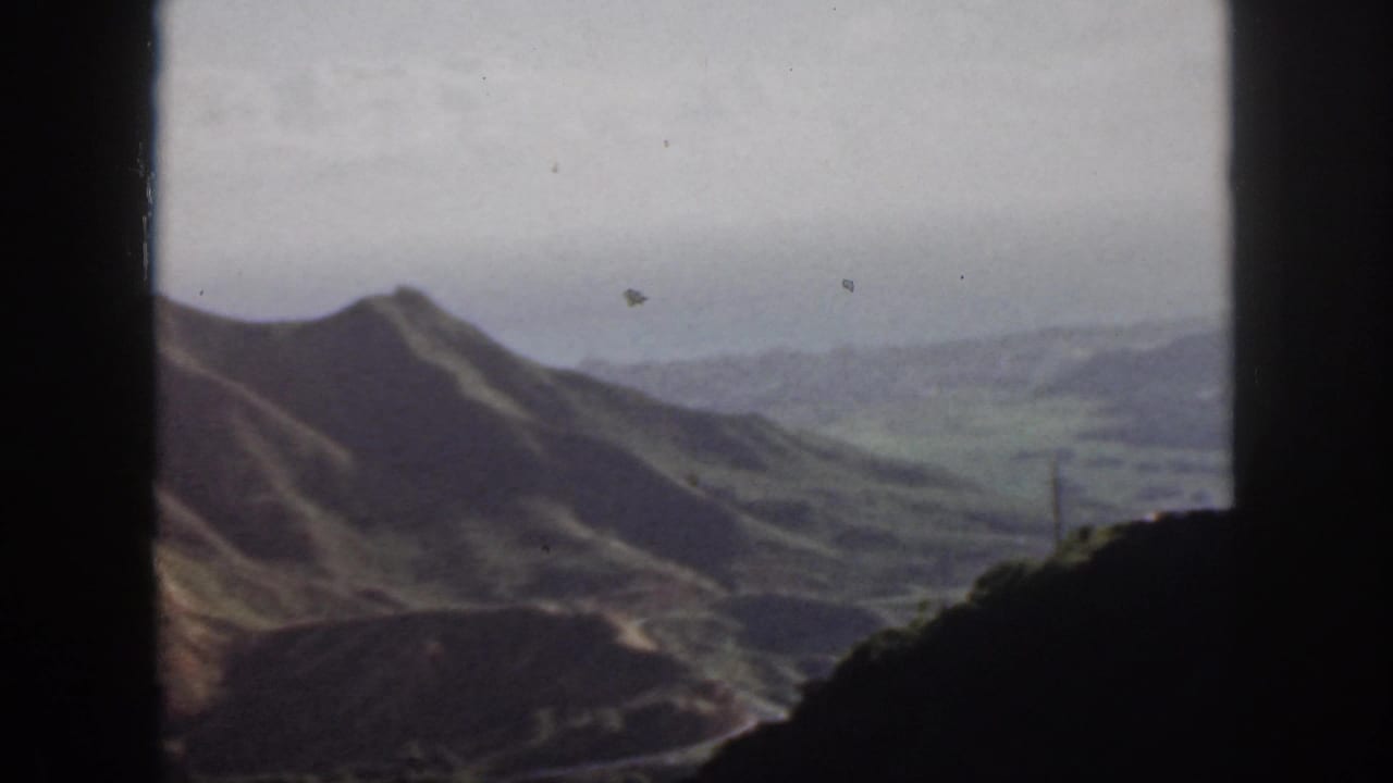 Vintage 8mm view of Oahu hills and a broad valley, with a road and utility pole faintly visible through the window frame.