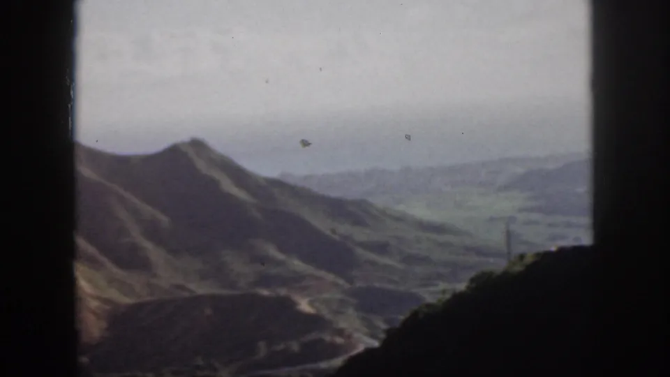 Vintage 8mm view of Oahu hills and a broad valley, with a road and utility pole faintly visible through the window frame.