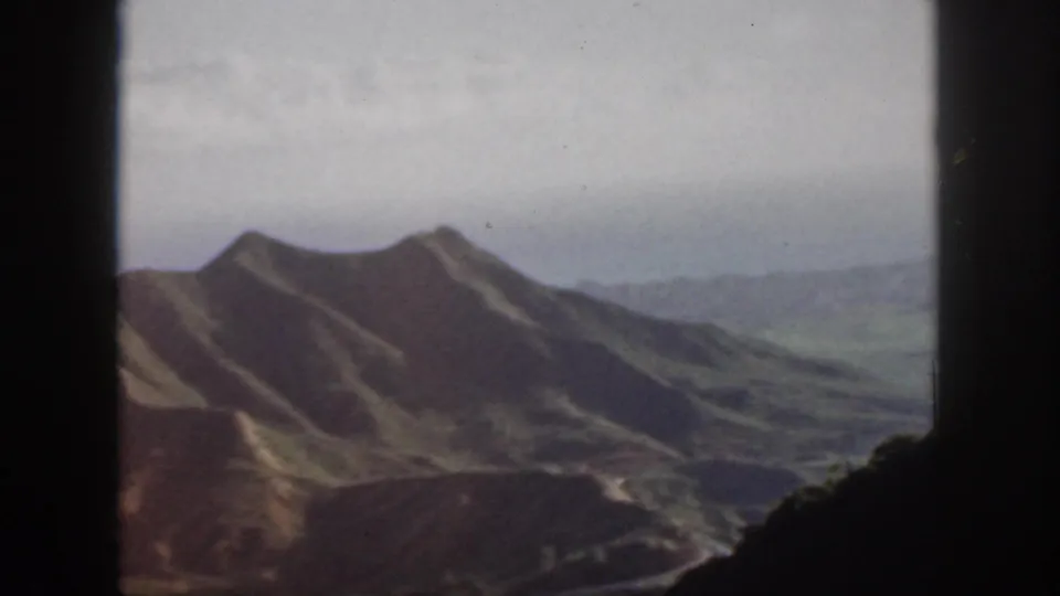 Oahu landscape in a 1959 8mm frame, with grassy ridges, distant valley land, and dark foreground framing.