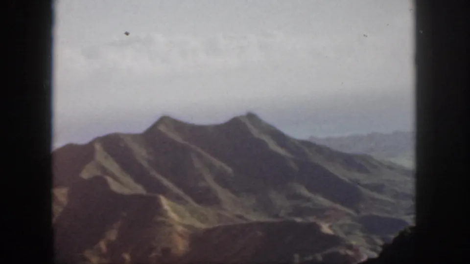 Final 1959 Oahu frame with grassy peaks, a hazy valley, and road traces bordered by dark window or lookout edges.