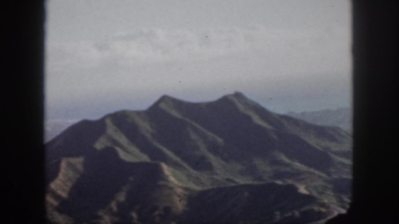 1959 Oahu 8mm view of rugged mountain ridges from the air, with distant haze and dark gate borders.