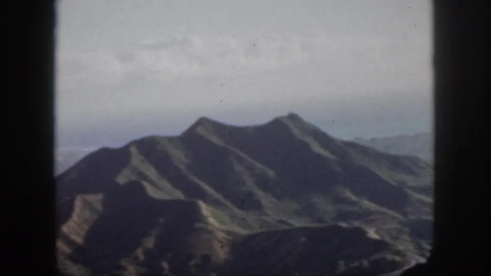 1959 Oahu 8mm view of rugged mountain ridges from the air, with distant haze and dark gate borders.