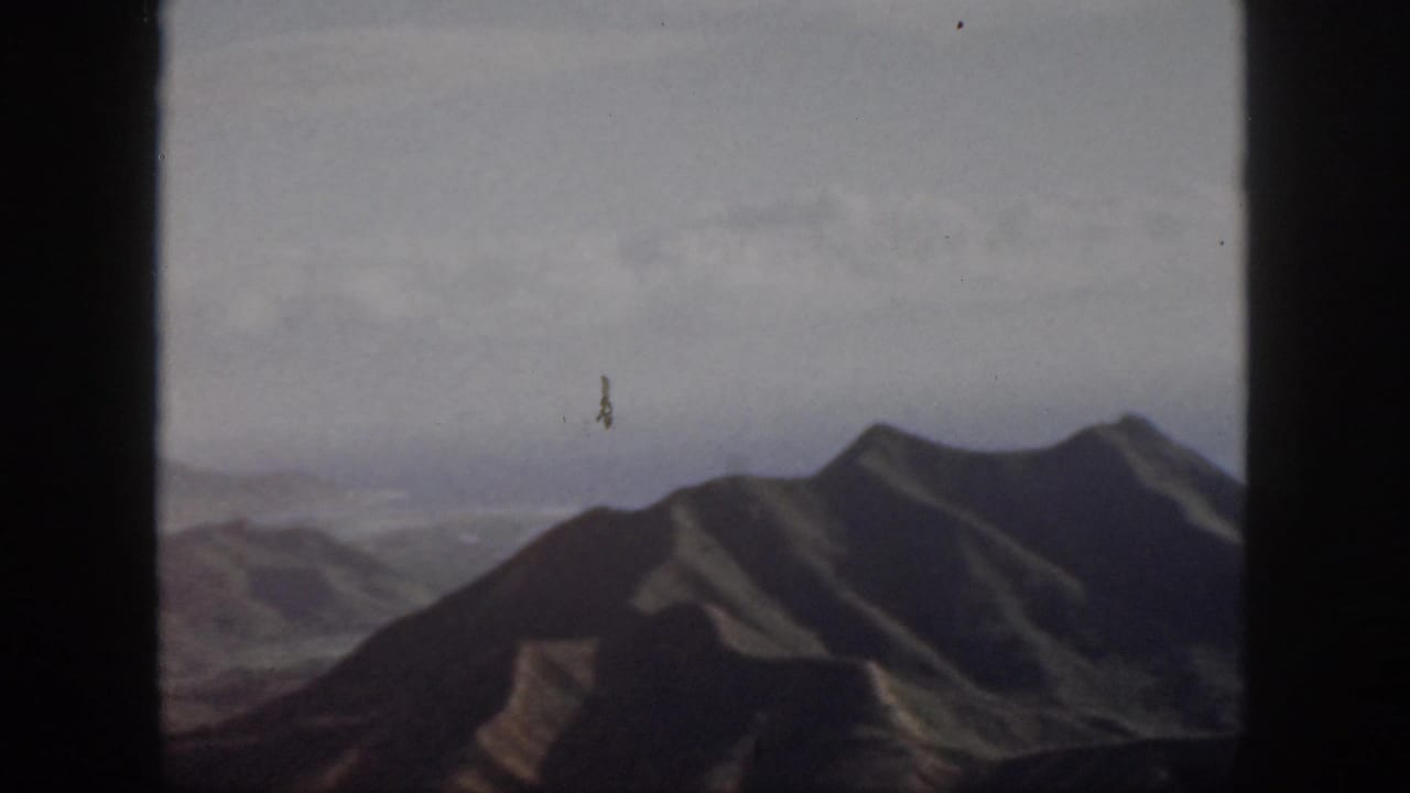 High mountain ridge with layered distant terrain and pale cloud cover.