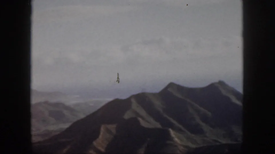 1959 Oahu aerial-style frame showing a dark ridgeline, distant valleys, and soft clouded sky on 8mm film.