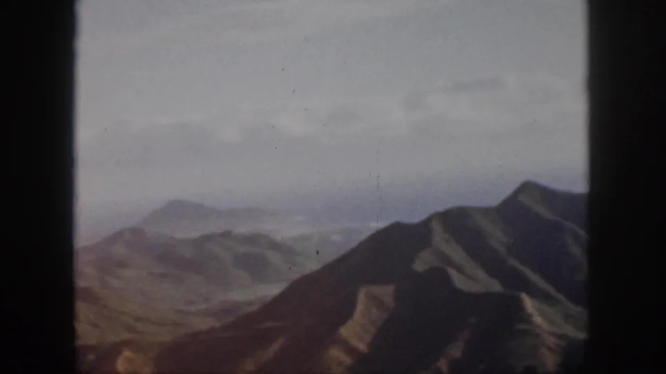 1959 Oahu 8mm frame with a broad foreground slope, distant hills, and softened sky haze from an airborne viewpoint.