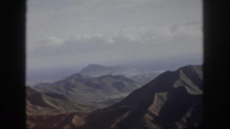1959 Oahu aerial view across a valley toward layered ridges, with faded 8mm color and visible frame borders.