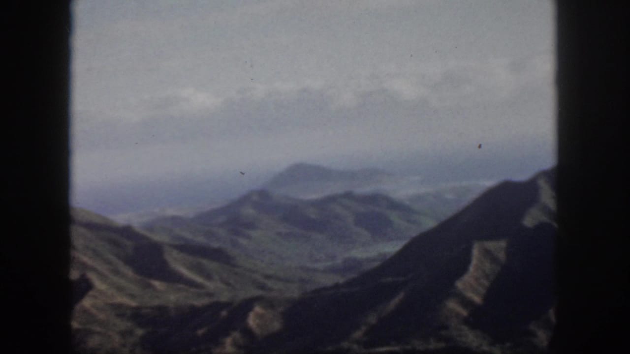 1959 Oahu home-movie view of layered mountain ridges and valleys beneath a pale, hazy sky.